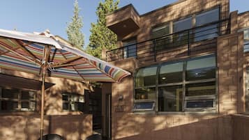 An outdoor seating area with a striped umbrella, brick walls, and large windows.
