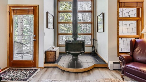 A cozy room with a wood-burning stove, large windows, a leather chair, and a small table.