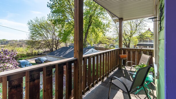A covered outdoor deck with a wooden railing, a table with chairs, and a view of a residential area with trees and parked cars. - Tremont - 2BR apt - Pet Friendly, Convenient to Stadiums, Clinic, Museums & more (Cleveland)