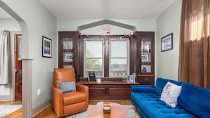 A living room with a brown leather chair, a blue sofa, a wooden coffee table, and a window with blinds. - Tremont - 2BR apt - Pet Friendly, Convenient to Stadiums, Clinic, Museums & more (Cleveland)