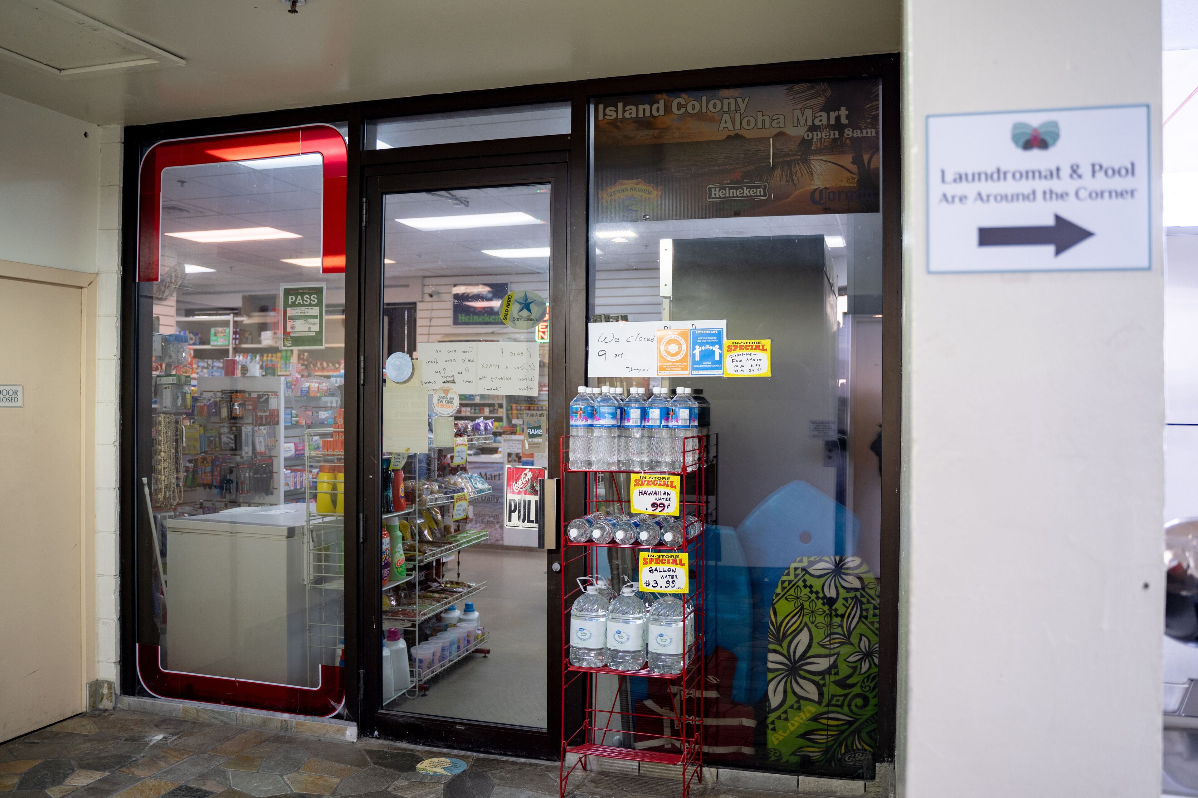 A store with a glass door, shelves stocked with bottled water, and signs indicating a laundromat and pool nearby.