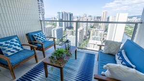 A balcony with blue furniture, a view of a cityscape, and a wooden table with a plant.
