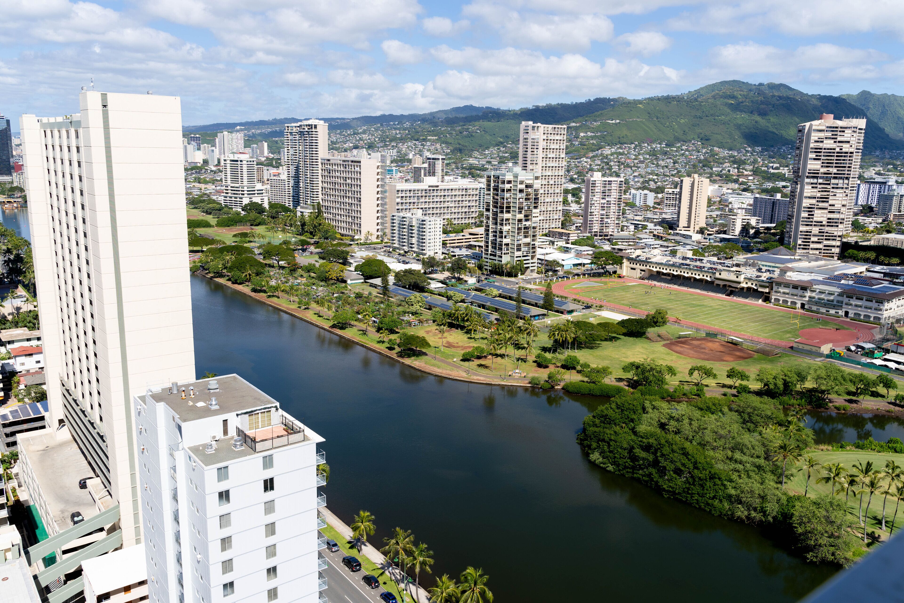 A cityscape with high-rise buildings, a river, and a sports field.