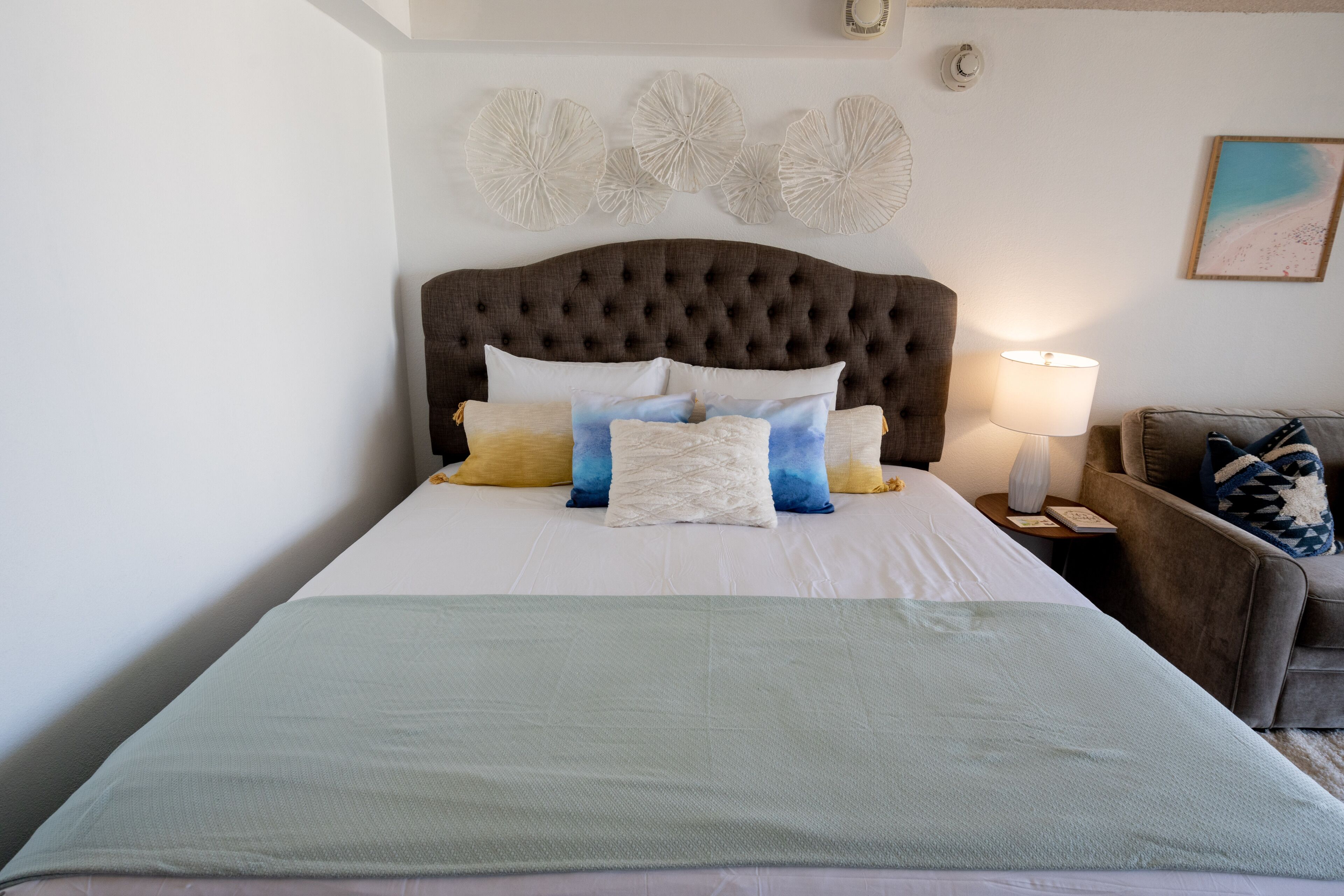 A neatly made bed with a tufted headboard, multiple pillows, and a light-colored blanket.