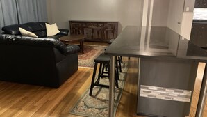 Ein modernes Wohnzimmer mit einer schwarzen Ledersofa, einem Holztisch und einer Küchenzeile mit schwarzer Arbeitsplatte und Hockern.