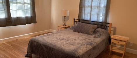 Un dormitorio con una cama, mesitas de noche de madera, una lámpara y cortinas translúcidas.