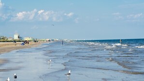 A beach with waves, people, and buildings in the background. - Sea Bliss - 3 bedroom, 2 bath home that sleeps 8 - Easy Beach Access! (Crystal Beach)