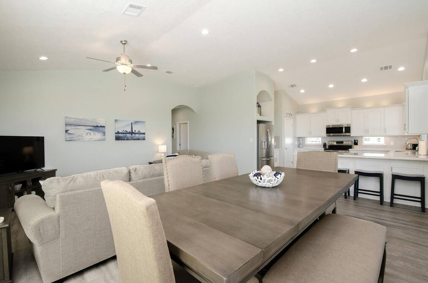 Un salon moderne avec une grande table à manger, des canapés de couleur beige et un ventilateur de plafond.
