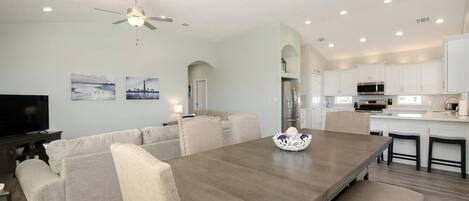 Un salon moderne avec une grande table à manger, des canapés de couleur beige et un ventilateur de plafond.