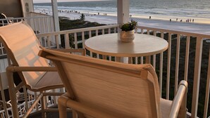 Un balcon avec vue sur la plage et l’océan, une table ronde avec un pot de fleurs et une chaise.