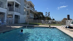 Une piscine à l’eau d’un bleu limpide, entourée d’une clôture blanche et bordée d’un bâtiment doté de balcons.