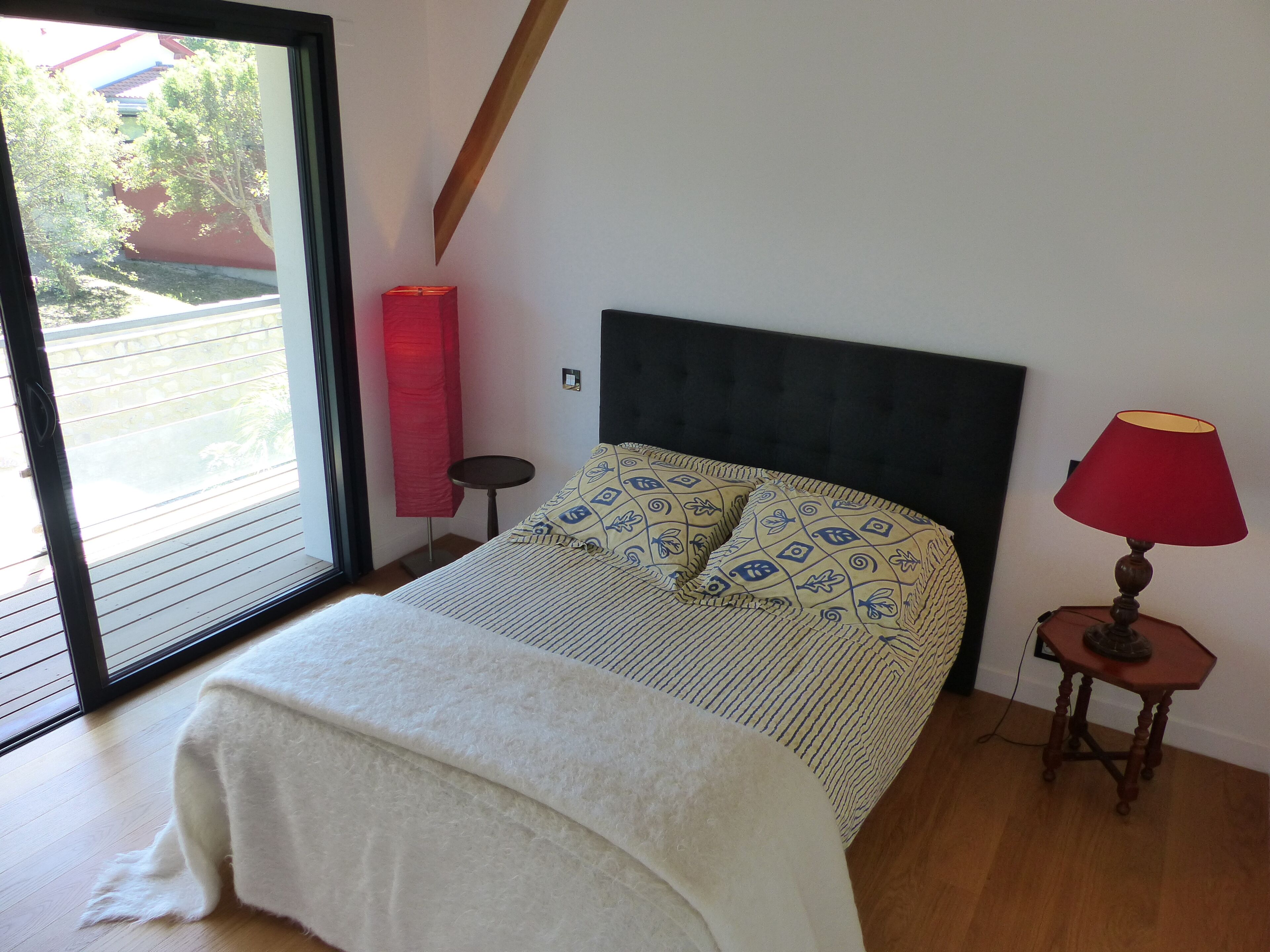 A bedroom with a bed, a window, a lamp, and a small table.