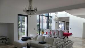 A spacious living room with a large sectional sofa, a chandelier, and a dining area with a red tablecloth. - Beautiful contemporary villa between lake and ocean. Free wifi. (Soorts-Hossegor)