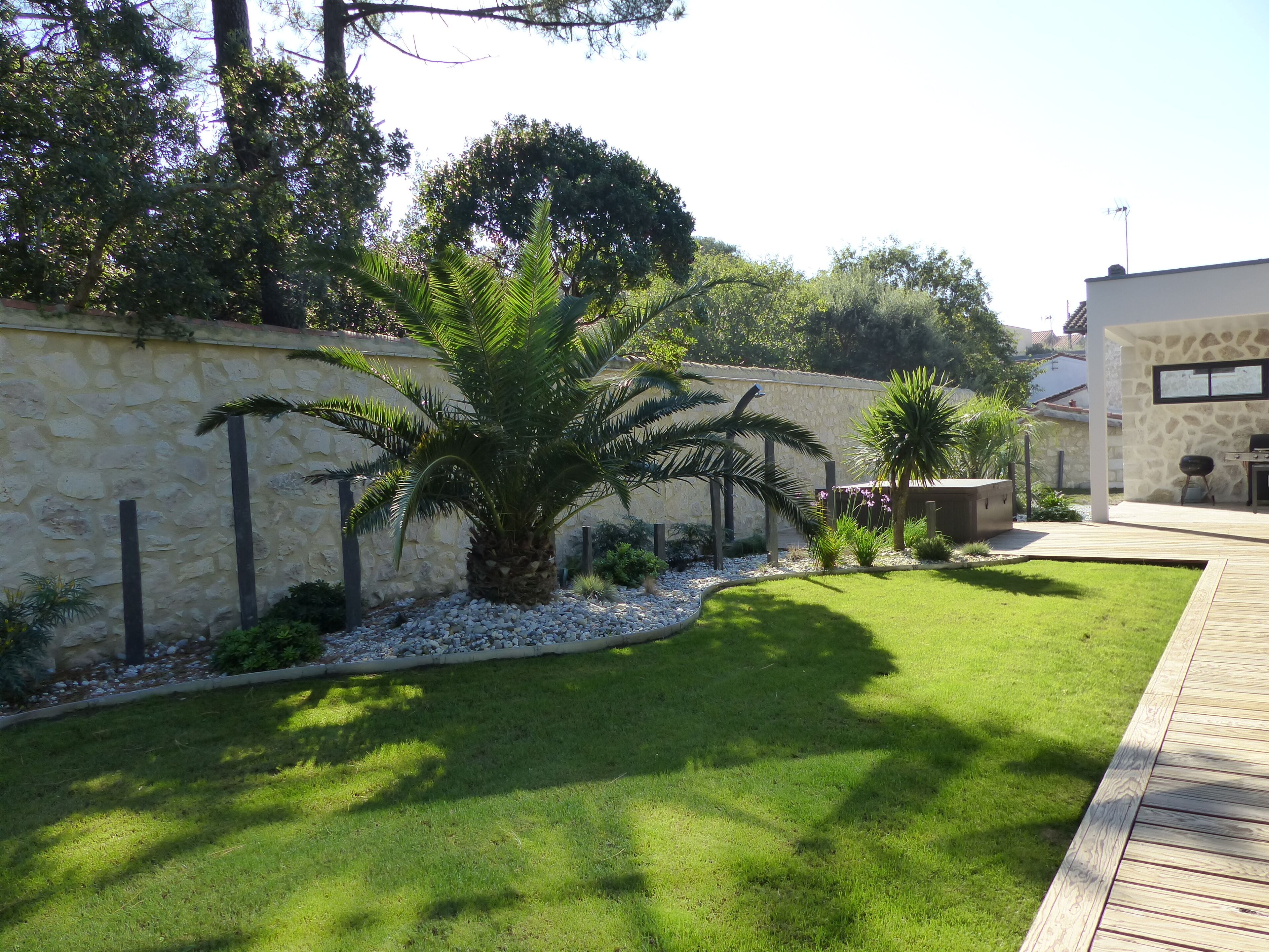 A well-maintained garden with a stone wall, palm trees, and a wooden deck.