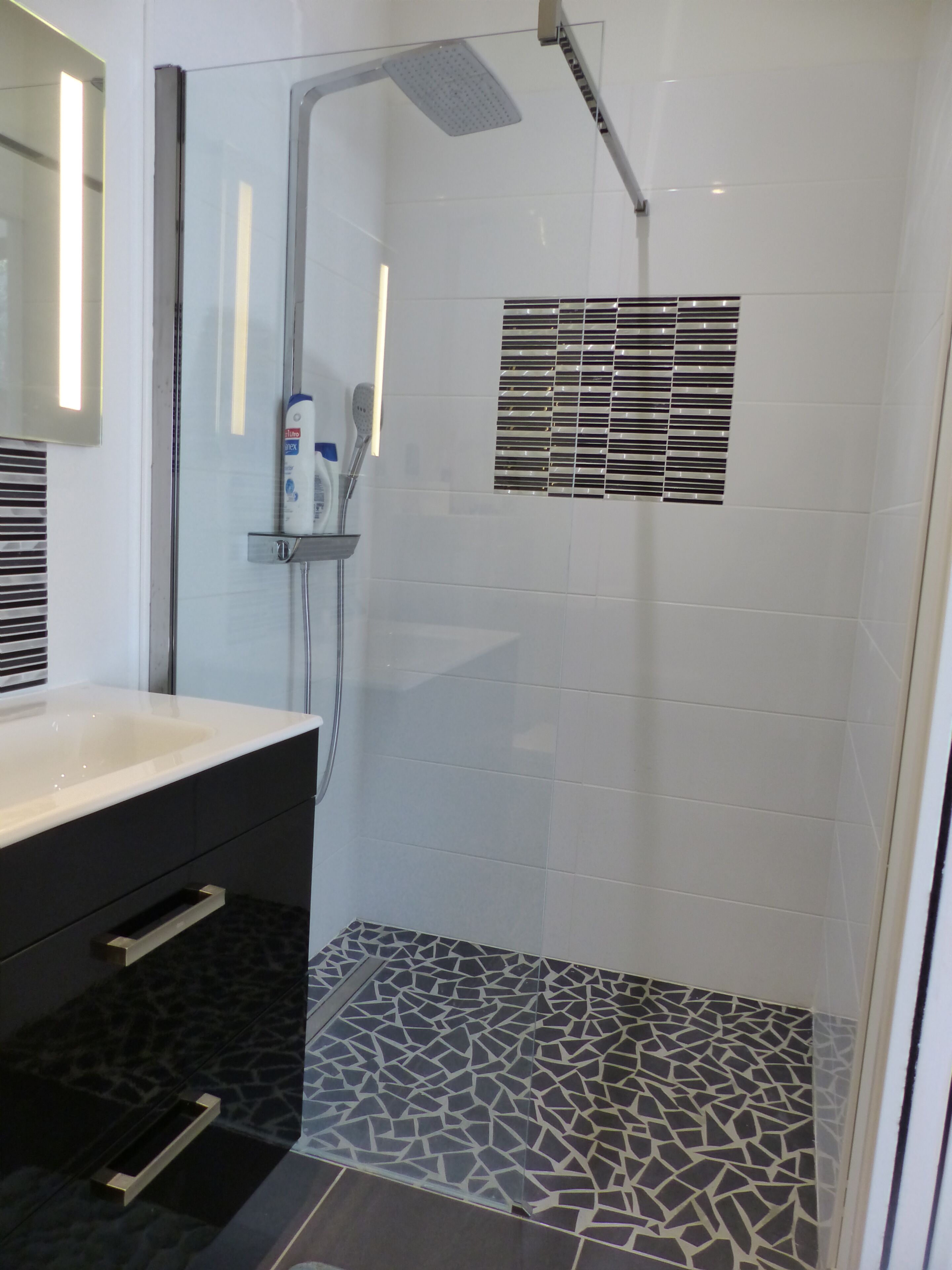 Ein modernes Badezimmer mit einer gläsernen Dusche, einem weißen Waschbecken und einem gemusterten Boden.