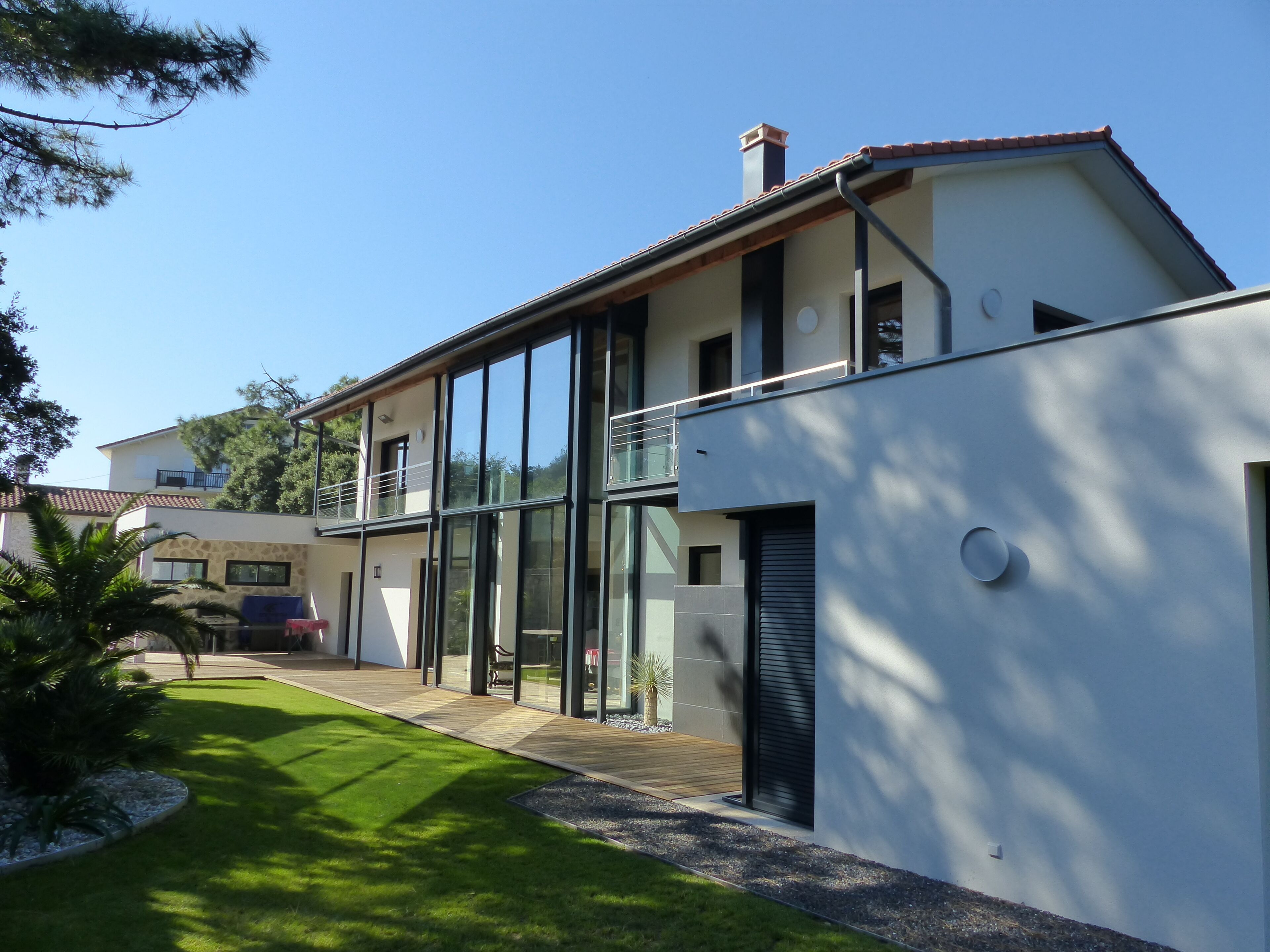 A modern two-story house with large windows, a balcony, and a well-maintained lawn.