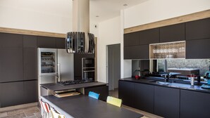 A modern kitchen with dark cabinetry, a central island with seating, and a built-in oven. - Beautiful contemporary villa between lake and ocean. Free wifi. (Soorts-Hossegor)