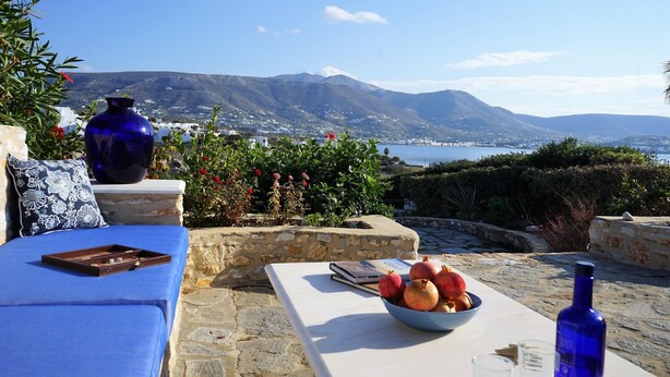 A terrace with a view of mountains, a table with a bowl of fruit, a blue vase, and a blue bottle. - Blue Paradise: Comfy Beach Villa walking distance to the sea / pool access (Paros)