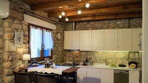 A rustic kitchen with stone walls, white cabinets, and a wooden ceiling. - Blue Paradise: Comfy Beach Villa walking distance to the sea / pool access (Paros)