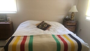 Una cama con edredón blanco y manta a rayas de colores.
