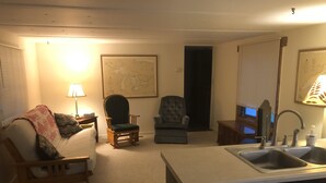 Un espacio habitable compacto con kitchenette, un sofá, dos sillones, un mapa en la pared y una lámpara.