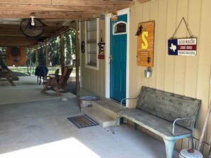 Une cabane rustique avec une porte bleue, une pancarte de bienvenue et un banc.