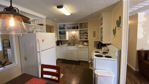 A compact kitchen with white appliances, wooden flooring, and a dining area with a star-patterned tablecloth. - Beautiful Country Home on 11 Acres Near Toledo Bend Lake. (Milam)