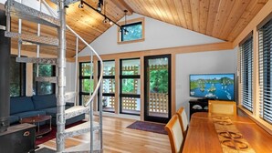 A spacious living room with a wooden staircase, large windows, a dining area, and a television. - Marblehead. Cottage on Whittier, new construction (Marblehead)