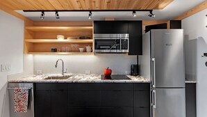 A modern kitchen with a black countertop, a stainless steel refrigerator, and a microwave above the sink. - Marblehead. Cottage on Whittier, new construction (Marblehead)