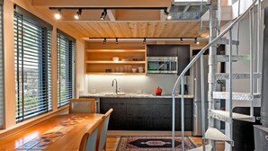 A modern kitchen with a central island, a dining area with a wooden table, and a spiral staircase. - Marblehead. Cottage on Whittier, new construction (Marblehead)