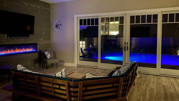Ein Wohnzimmer mit integriertem Kamin, einer Couch und einer Glastür, die zu einem Poolbereich führt.