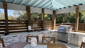 Eine Terrasse im Freien mit einem Holztisch und -stühlen, einer Steinarbeitsplatte mit Grill und einem Holzzaun.