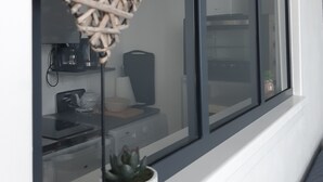 Huoneessa on suuri ikkuna, seinäkello, punottu sydämenmuotoinen koriste, ruukkukasvi ja keittiökoneita.