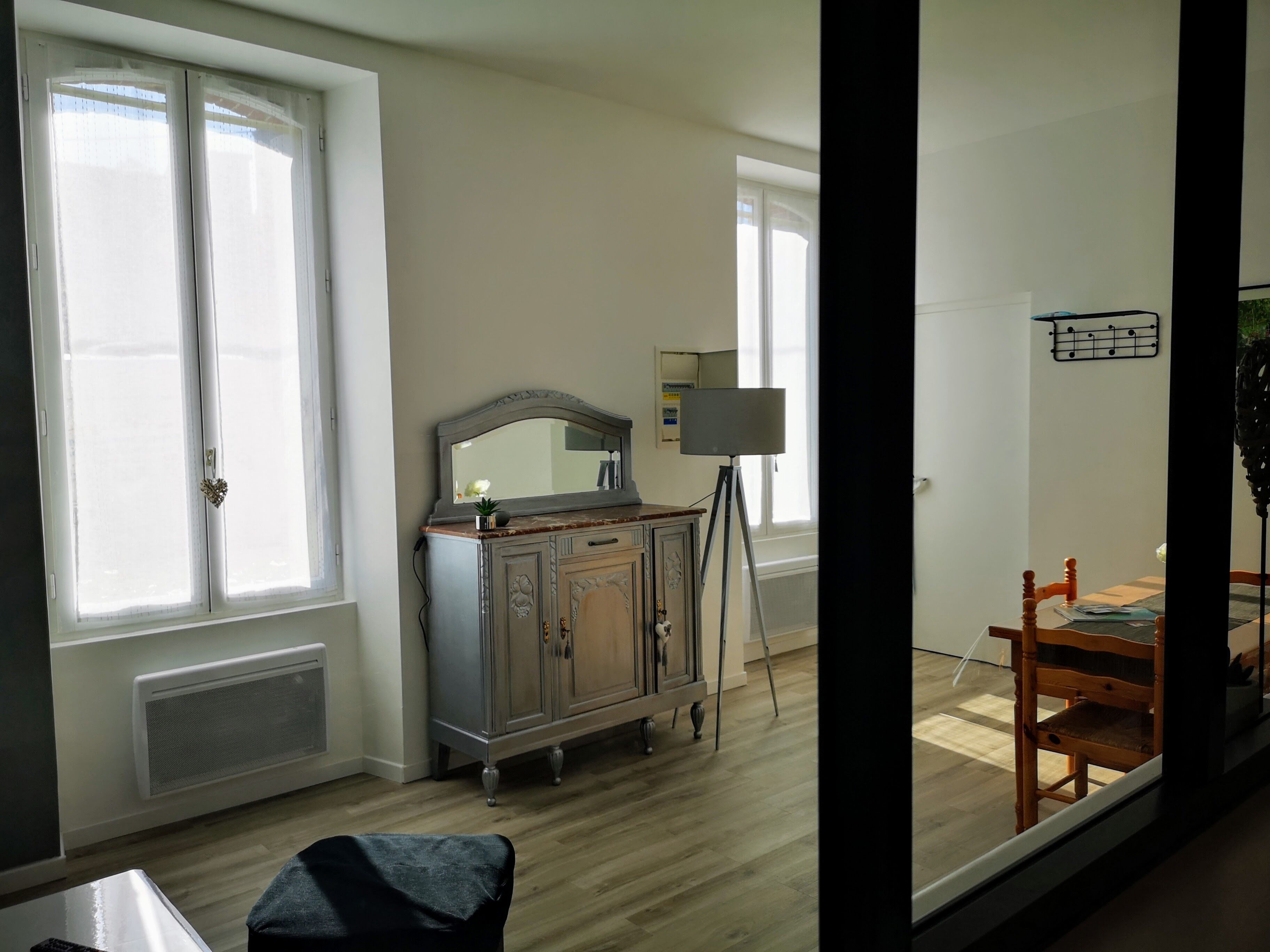 A room with a wooden floor, a dresser with a mirror, a lamp on a tripod, and a chair.