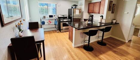 A modern kitchen with a central island, bar stools, and a dining table with chairs.