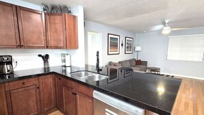 A kitchen with wooden cabinets, a black countertop, a dishwasher, and a dining area with a couch and table. - Mo`s Mid-Town 2Bdrm Marvel 103 (Phoenix)