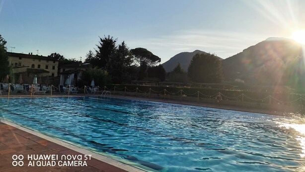 A swimming pool with clear water, surrounded by lounge chairs and umbrellas, with mountains in the background and a clear sky. - Villetta Camelia with private parking just a stone's throw from Lucca (Capannori)