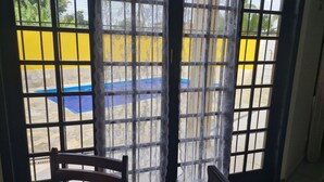 A room with a view of a pool through a window with a lace curtain. - Beach house: 5 bedrooms, swimming pool, barbecue, billiards. Excellent location. (Bertioga)