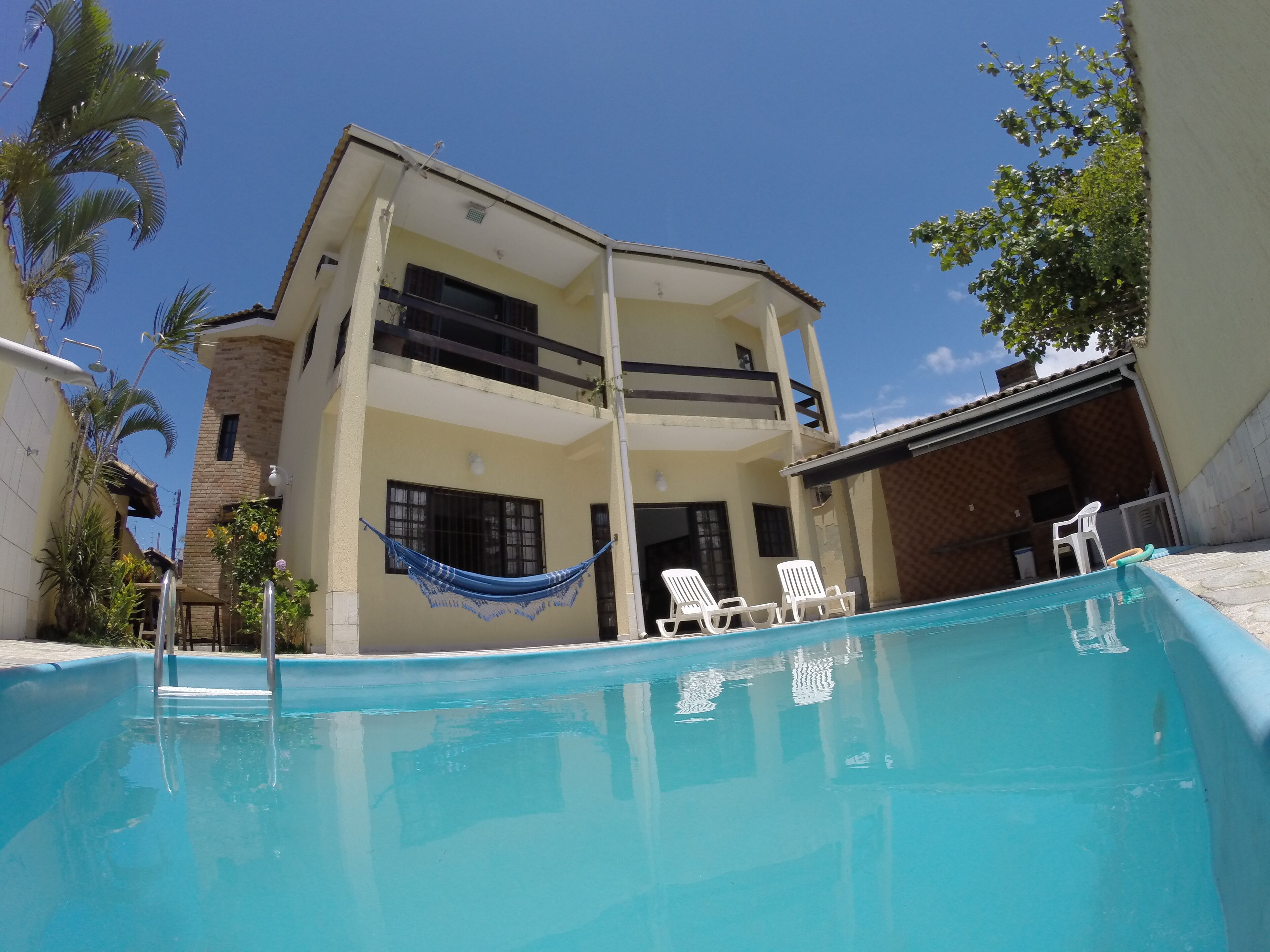 A two-story building with a swimming pool, white lounge chairs, and a hammock.