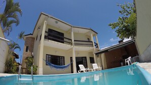 A two-story building with a swimming pool, white lounge chairs, and a hammock. - Beach house: 5 bedrooms, swimming pool, barbecue, billiards. Excellent location. (Bertioga)