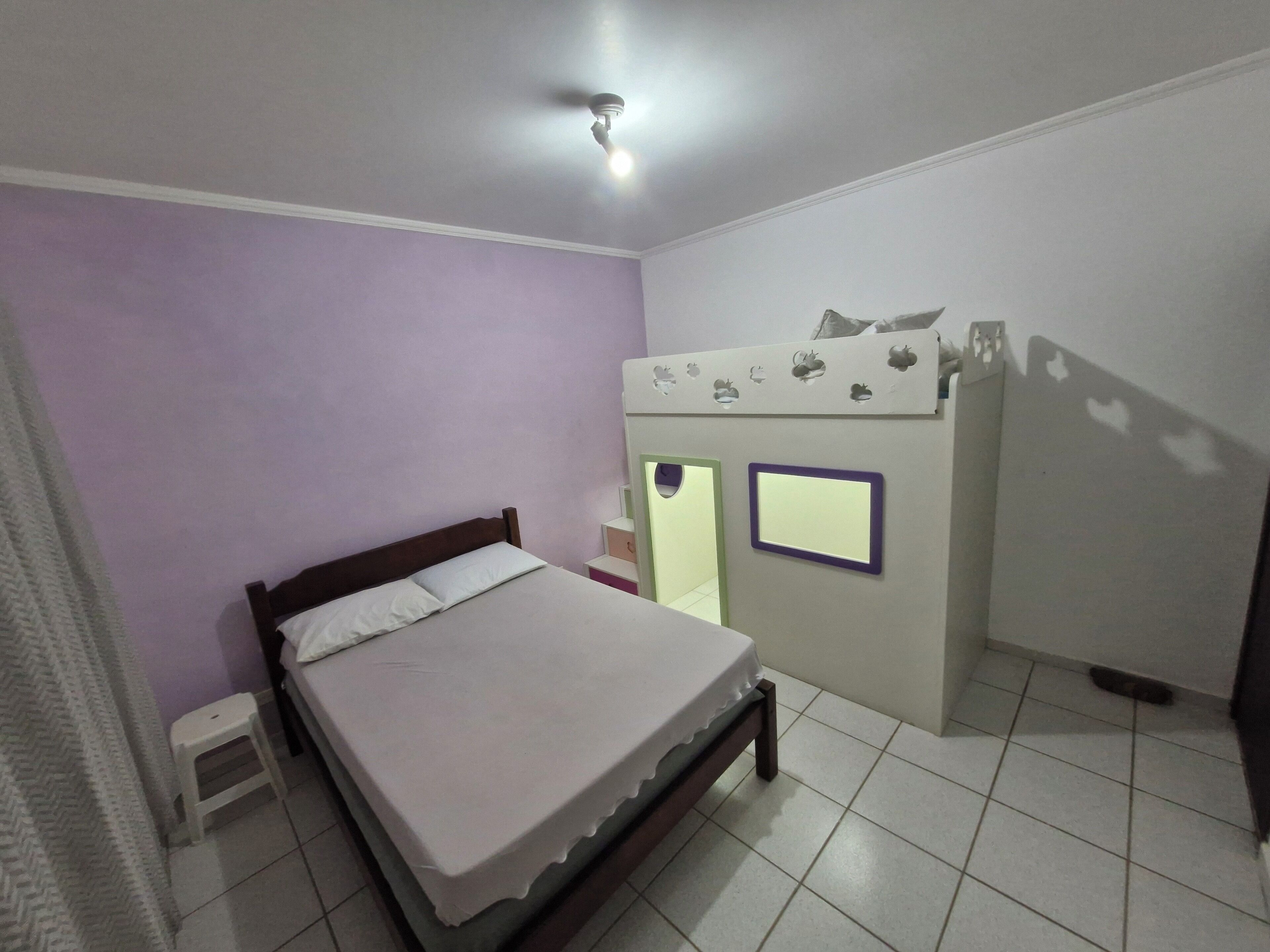 Un dormitorio con cama, un taburete pequeño, un armario y un ventilador de techo.