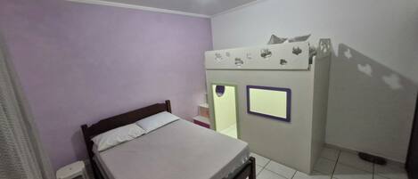 Un dormitorio con cama, un taburete pequeño, un armario y un ventilador de techo.