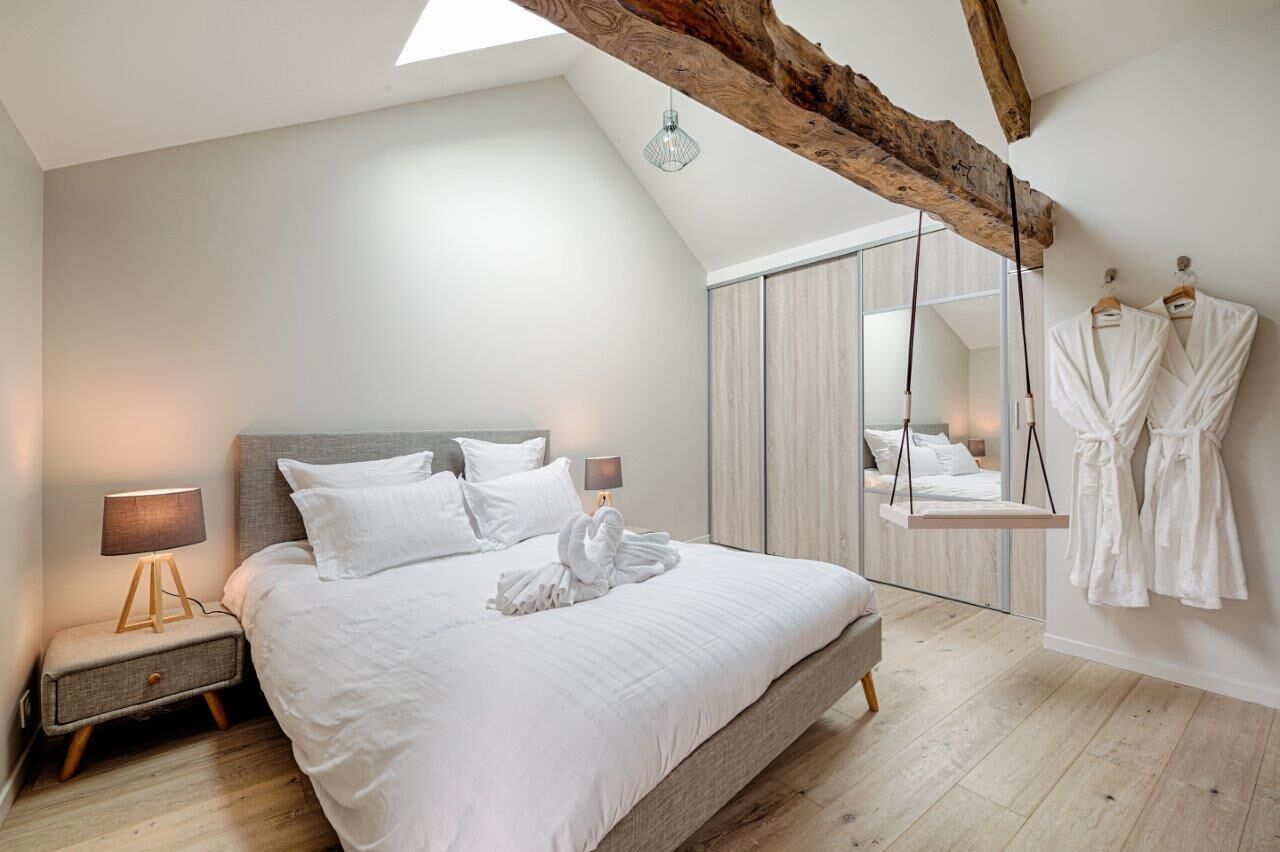 A modern bedroom with a large bed, a nightstand, a hanging robe rack, and a wooden ceiling beam.