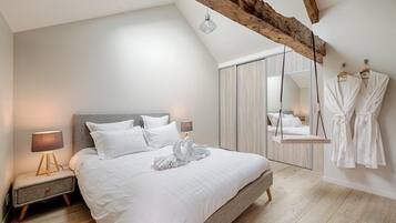 A modern bedroom with a large bed, a nightstand, a hanging robe rack, and a wooden ceiling beam.
