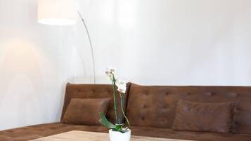 Eine weiße Vase mit einer Orchidee auf einem Holztisch vor einer braunen Ledercouch.