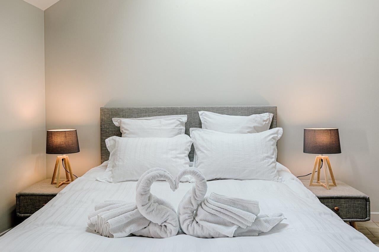 Un lit bien fait, avec du linge de lit blanc et des oreillers, deux lampes de chevet et des serviettes disposées en forme de cœur sur le lit.