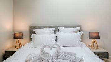 Un lit bien fait, avec du linge de lit blanc et des oreillers, deux lampes de chevet et des serviettes disposées en forme de cœur sur le lit.