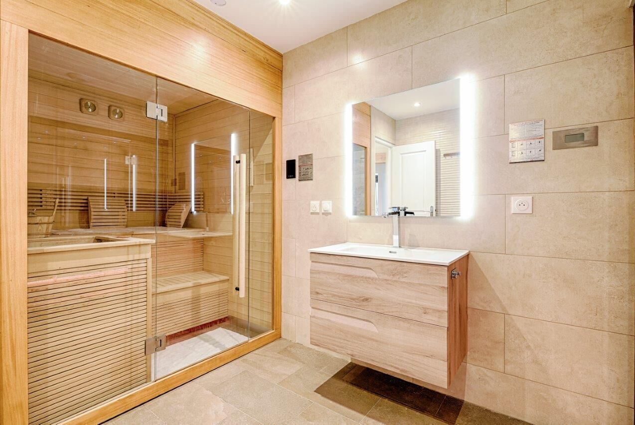 Une salle de bain moderne dotée d’une douche à parois de verre, de lambris en bois, d’un grand miroir et d’un lavabo avec un meuble-vasque en bois.