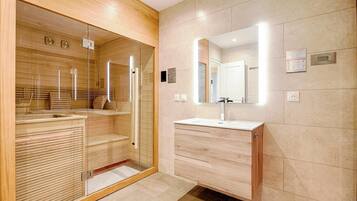 Une salle de bain moderne dotée d’une douche à parois de verre, de lambris en bois, d’un grand miroir et d’un lavabo avec un meuble-vasque en bois.