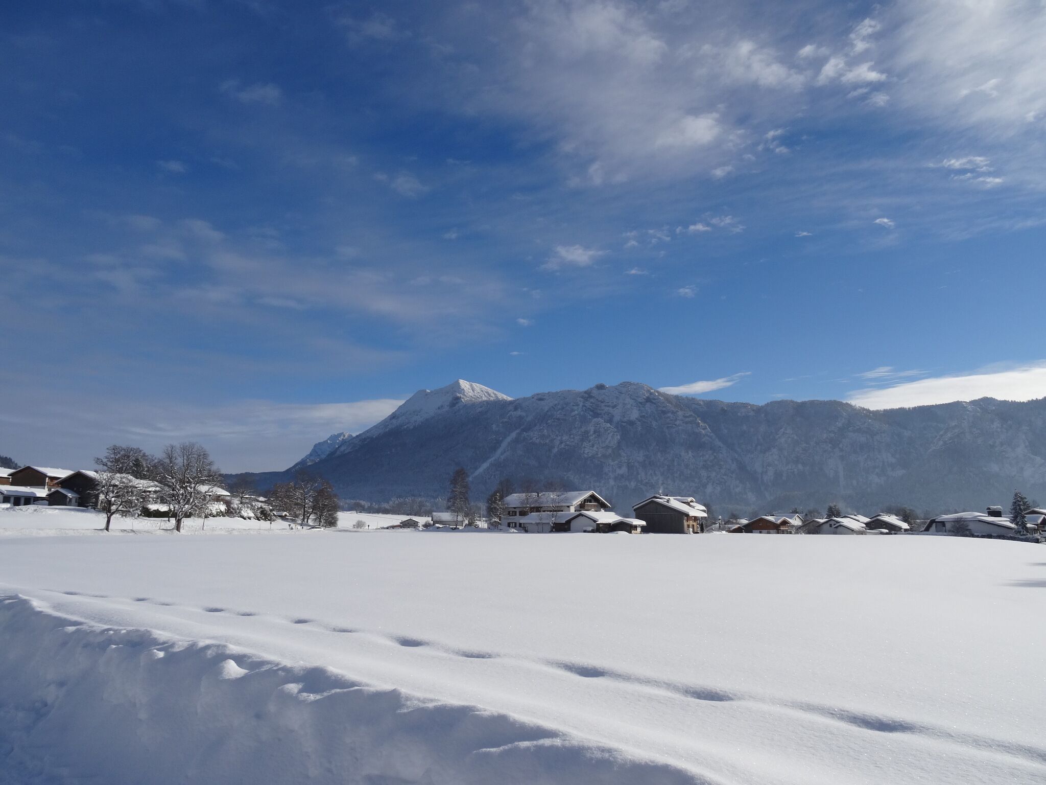 Eine verschneite Berglandschaft mit Häusern im Vordergrund und einem Berg im Hintergrund.
